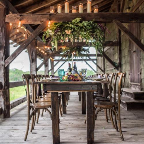 A rustic dining setup with a wooden table, chairs, and a floral centerpiece, illuminated by candles and string lights.
