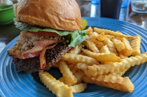 A close-up of a burger with bacon, lettuce, and tomato, served with a side of crinkle-cut fries on a blue plate.