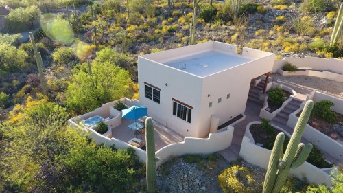 Aerial view of a modern white house surrounded by desert vegetation and cacti, featuring a patio and outdoor seating.