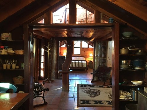 Cozy interior of a rustic cabin with wooden beams, a living area, and a kitchen space filled with pots and utensils.