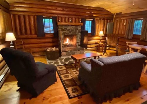 Cozy log cabin interior with a stone fireplace, wooden furniture, and warm lighting.