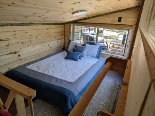 Cozy loft bedroom with a large bed, wooden walls, and a window overlooking a deck.