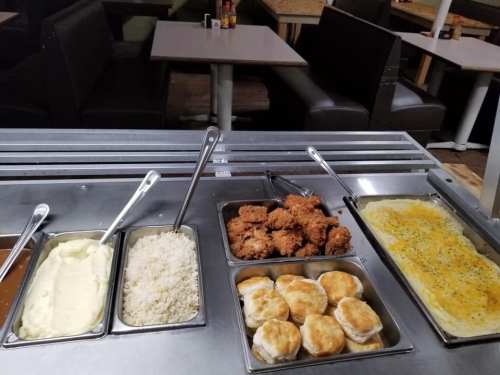 A buffet spread featuring mashed potatoes, rice, fried chicken, biscuits, and a cheesy casserole in metal trays.
