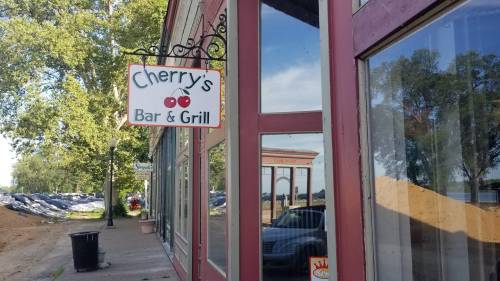 Sign for "Cherry's Bar & Grill" on a building, with trees and a parking area visible in the background.