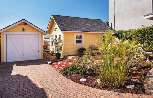 A charming yellow house with a white garage, surrounded by landscaped gardens and a brick pathway.