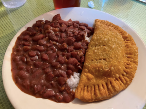 A plate with rice topped with red beans and a golden-brown empanada on the side.