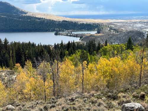 Scenic view of a lake surrounded by autumn trees and mountains under a cloudy sky.