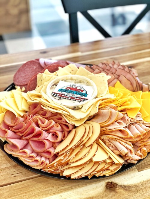 A colorful platter of assorted deli meats and cheeses, featuring a central dip container.