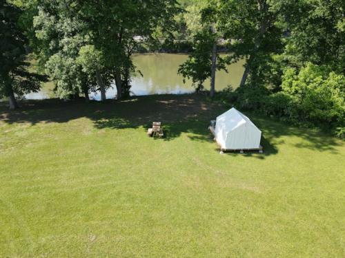 Aerial view of a grassy area with a tent and a chair near a calm river surrounded by trees.
