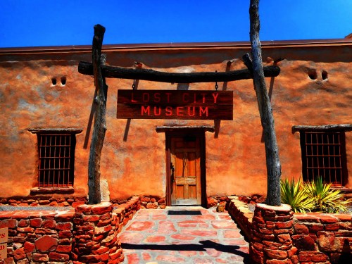 Entrance to the Lost City Museum, featuring a wooden sign and adobe-style architecture under a clear blue sky.