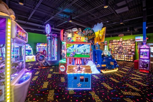 Brightly lit arcade filled with colorful games, plush toys, and vibrant carpet, creating a fun, playful atmosphere.