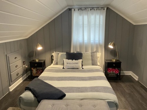 Cozy attic bedroom with a striped bedspread, two bedside lamps, and a welcoming decorative pillow.