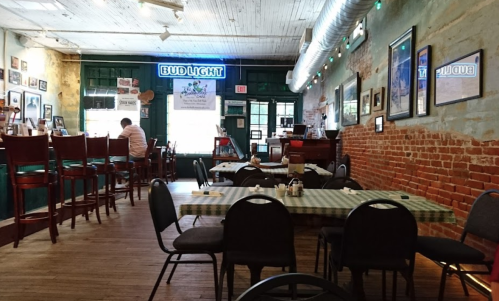 Interior of a rustic restaurant with wooden floors, brick walls, and tables set with checkered tablecloths.