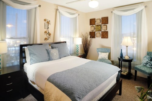 Cozy bedroom with a queen bed, decorative pillows, two lamps, and a seating area by the window. Soft lighting and decor.