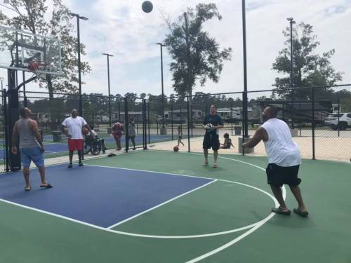 Four people playing basketball on an outdoor court, with one shooting the ball while others watch.
