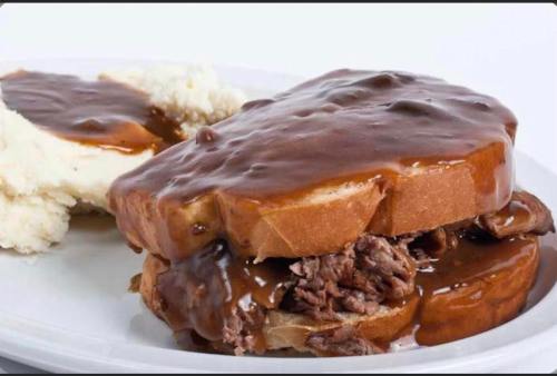 A plate featuring a beef sandwich with gravy on bread, accompanied by a side of mashed potatoes.