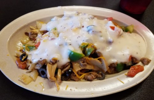 A plate of nachos topped with ground meat, cheese, olives, peppers, and a creamy white sauce.