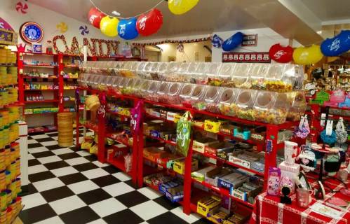 A colorful candy store interior with red shelves filled with jars of sweets and a checkered black-and-white floor.