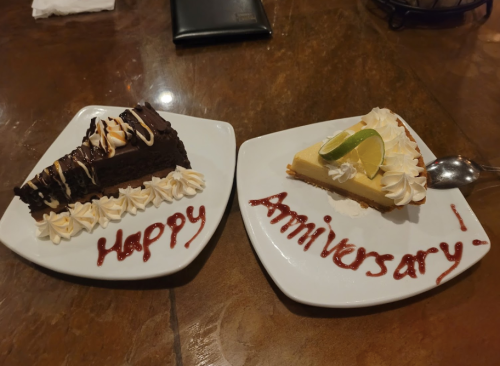 Two dessert plates: one with chocolate cake and the other with key lime pie, both decorated with "Happy Anniversary" in sauce.