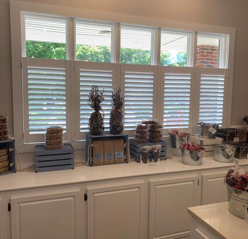 A kitchen counter with decorative items, including baskets and containers, under window shutters.