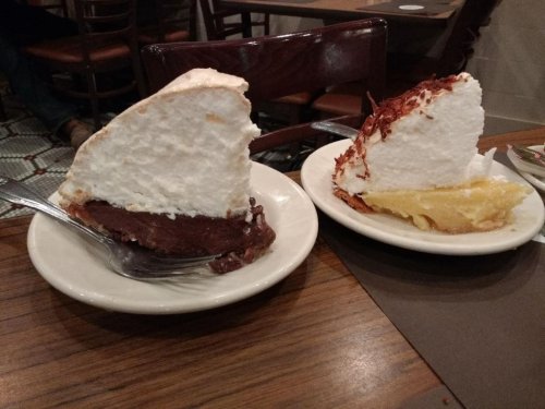 Two slices of pie on plates: one chocolate with meringue topping, the other lemon with a fluffy white topping.