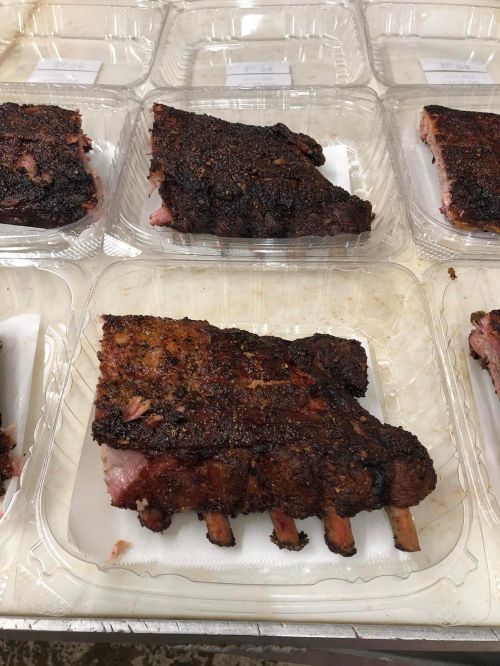 Plates of smoked ribs with a dark, crispy crust, arranged neatly on a table.