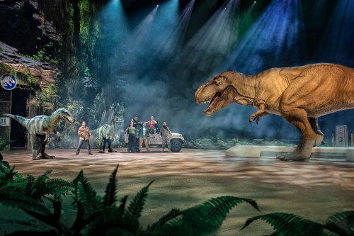 A dinosaur-themed show featuring a T. rex, actors, and vehicles in a misty, jungle-like setting.