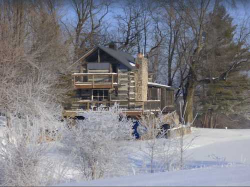 A cozy log cabin surrounded by snow-covered trees and a frosty landscape on a clear winter day.