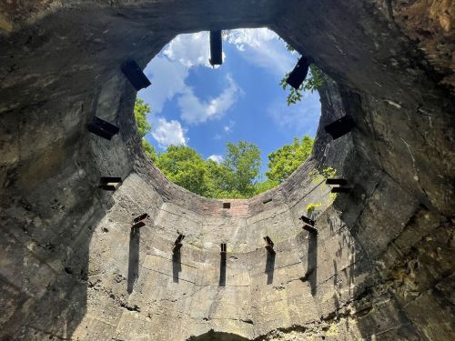 View from inside a circular stone structure, looking up at a blue sky with scattered clouds and greenery around the edges.