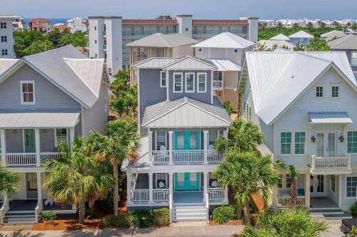 Aerial view of coastal homes with palm trees, featuring a central house with a light blue door and white siding.