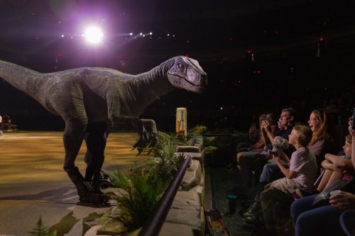 A lifelike dinosaur animatronic interacts with an excited audience at a live show.