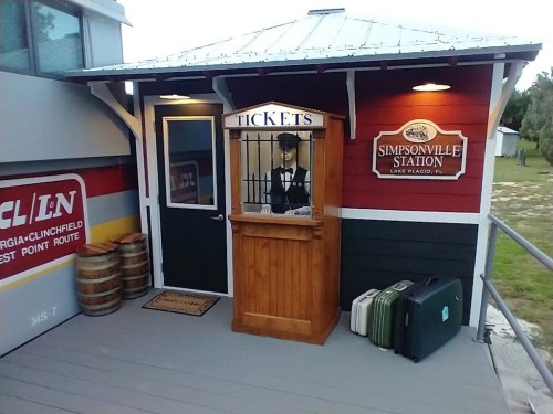 A vintage ticket booth at Simpsonville Station, featuring a mannequin in period attire and old suitcases nearby.
