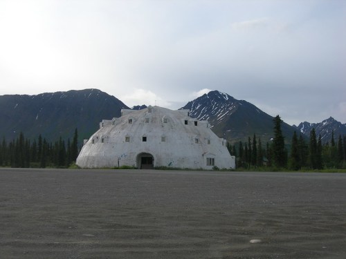 A large, white, dome-shaped structure in a remote landscape with mountains and trees in the background.