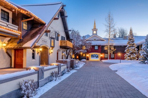 Charming winter scene of a snow-covered village with festive lights, cozy buildings, and a clock tower in the background.