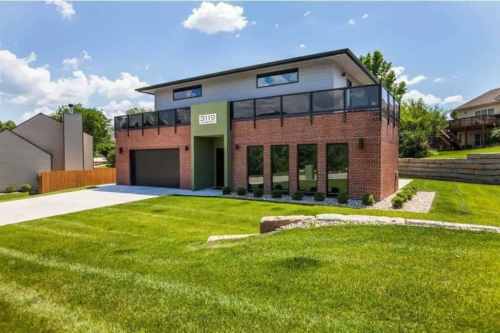 Modern two-story house with a green accent, large windows, and a spacious lawn under a blue sky.