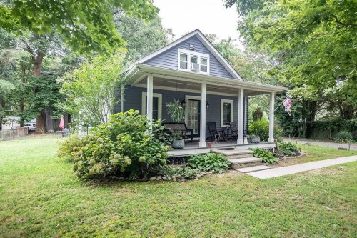 A charming blue house with a front porch, surrounded by greenery and a well-kept lawn.