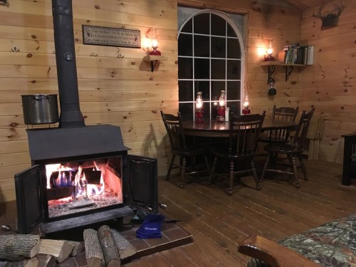 Cozy cabin interior with a wood stove, dining table, and candles, creating a warm, inviting atmosphere.