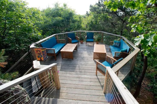 A wooden deck surrounded by trees, featuring blue chairs and tables for outdoor seating.