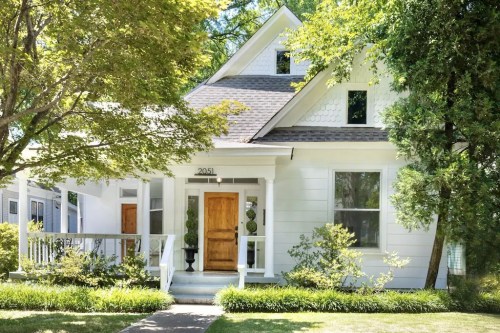 Charming white house with a wooden door, surrounded by greenery and a welcoming front porch.