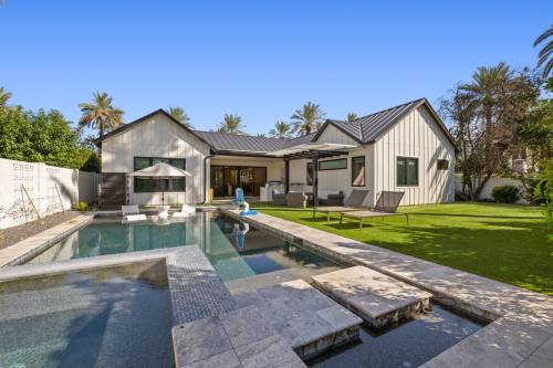 Modern house with a pool, surrounded by palm trees and a well-maintained lawn, featuring outdoor seating and a patio.