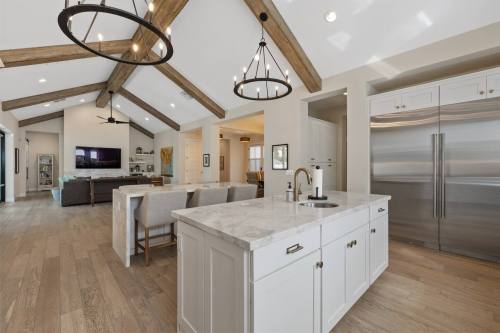 Modern kitchen with a marble countertop, open layout, wooden beams, and stainless steel appliances in a bright living space.