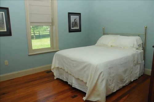 A simple bedroom with a light blue wall, a bed covered in a white blanket, and framed pictures on the walls.