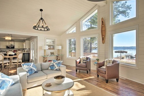 Bright, airy living room with large windows, modern furniture, and a view of a lake outside.