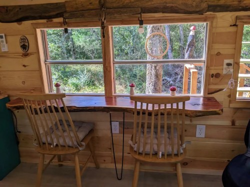 A cozy wooden table with two chairs by a large window overlooking a forested area.