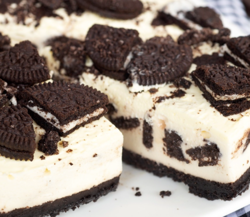 Close-up of a creamy cheesecake topped with crushed Oreos and cookie pieces on a white plate.