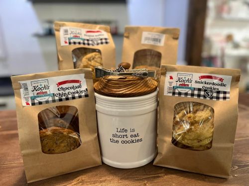A jar with "Life is short eat the cookies" surrounded by cookie packages: chocolate chip and snickerdoodle.