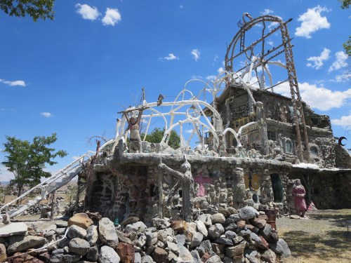 A whimsical stone structure with sculptures and arches, set against a blue sky with scattered clouds.