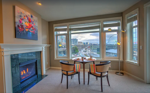 Cozy corner with a fireplace, two chairs, and a view of a cityscape featuring a Ferris wheel and cloudy sky.