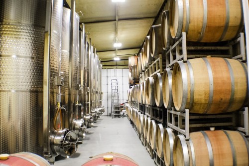 Interior of a winery featuring stainless steel tanks and wooden barrels stacked on racks.