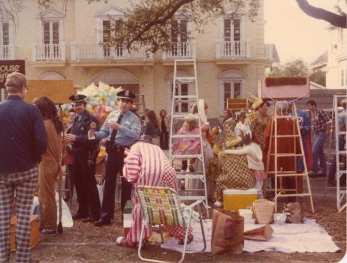 A lively outdoor scene with police officers, clowns, and people enjoying a festive atmosphere in a park setting.